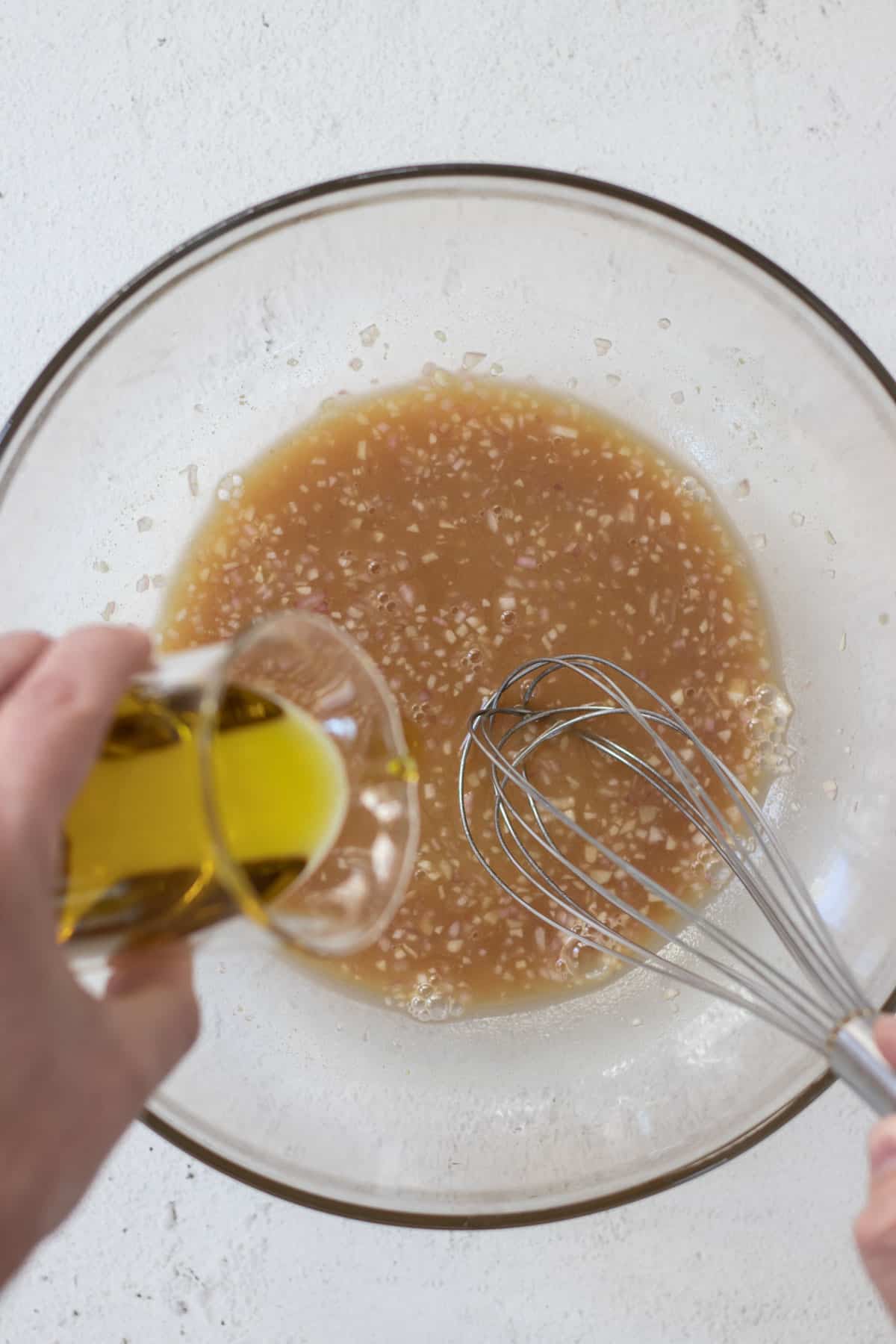 Whisking olive oil into dressing inside of a large glass bowl.