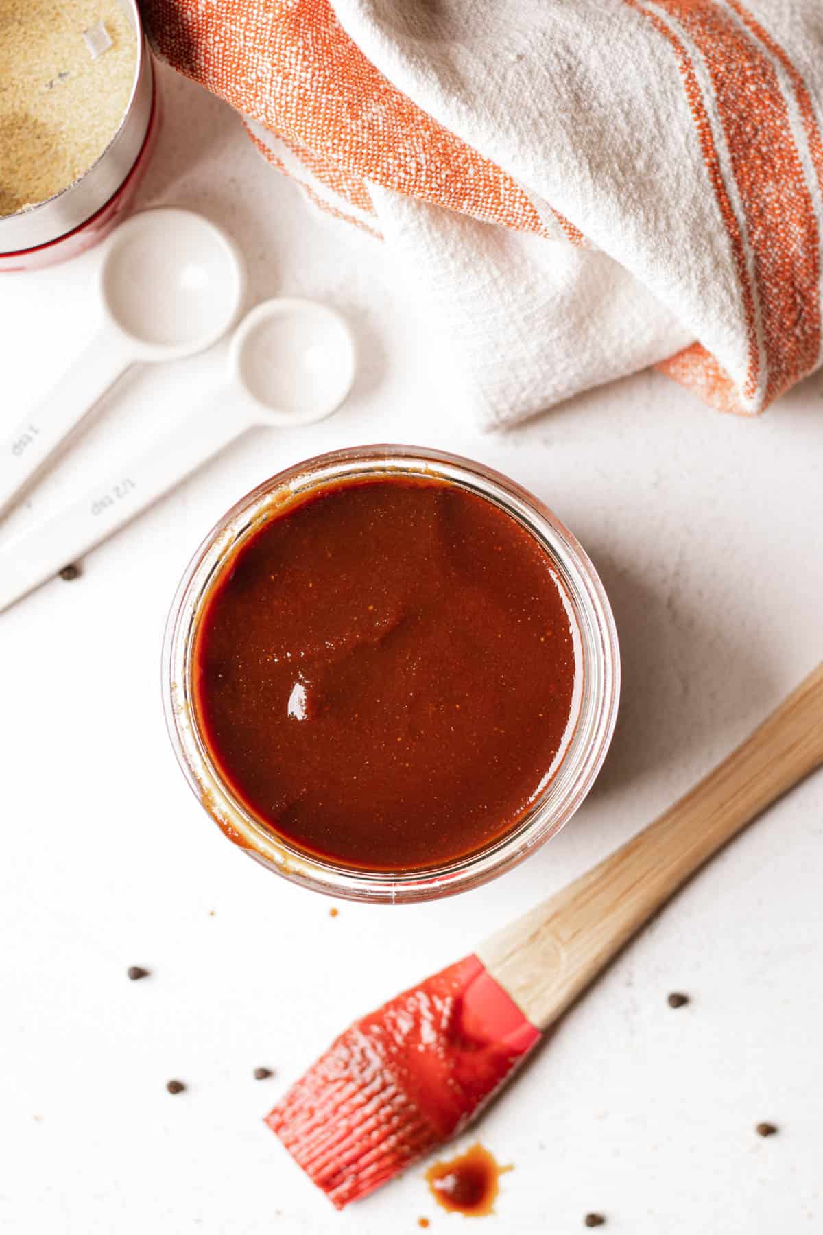 Overhead photo of bbq sauce in a small glass jar with a brush covered in bbq sauce.