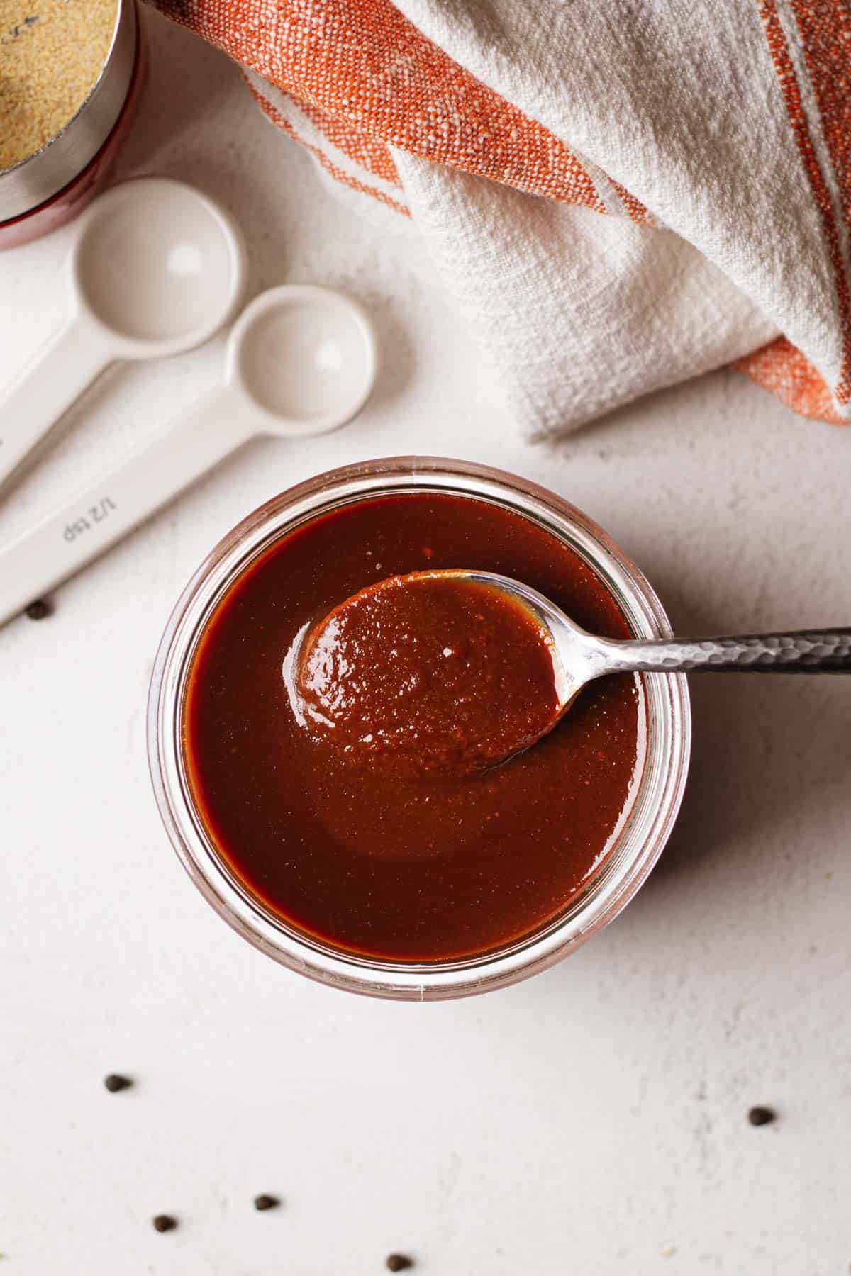 Overhead picture of a spoon being dipped in a jar of bbq sauce.
