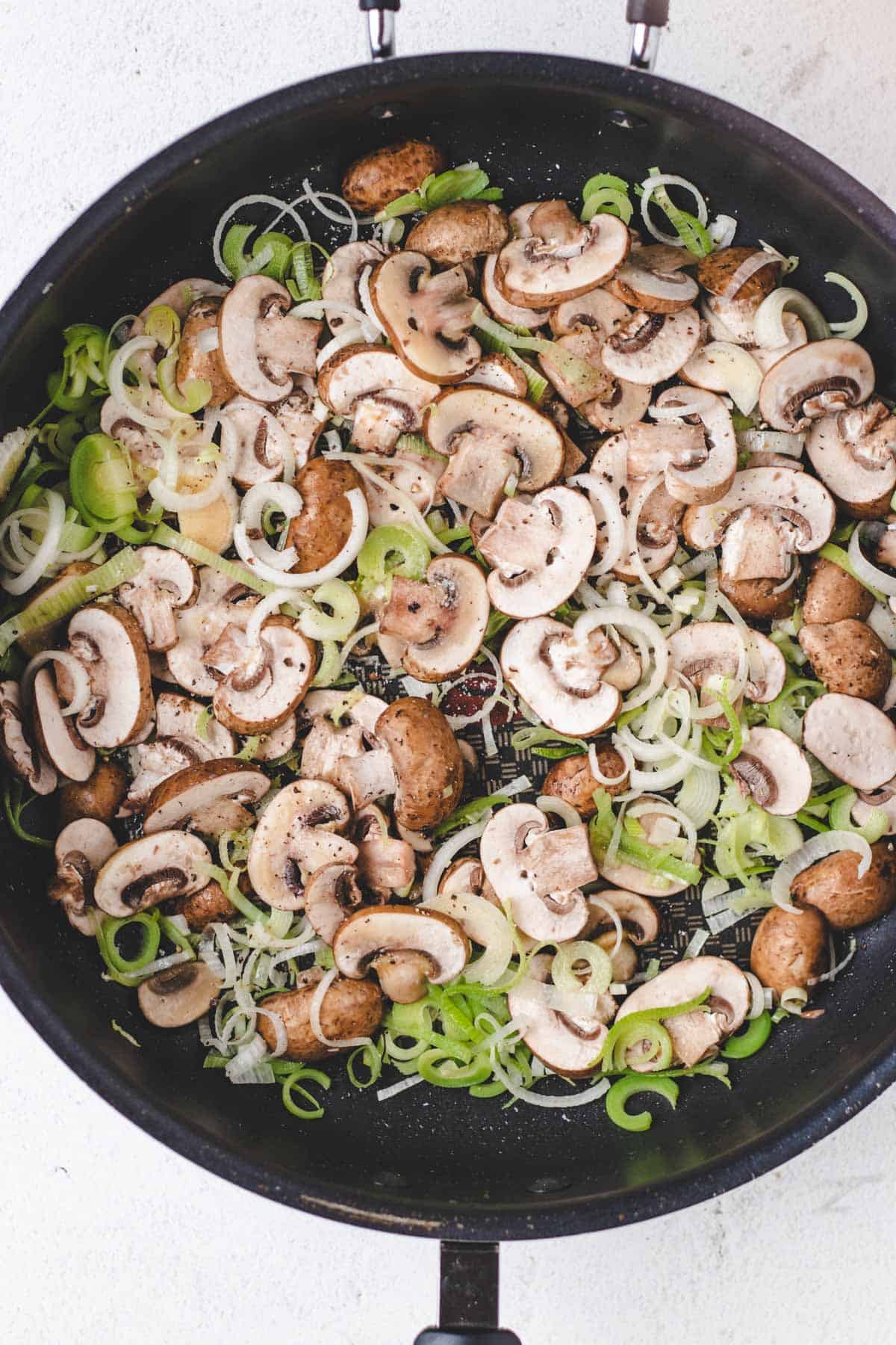 Cooking sliced mushrooms and leeks in a large cast iron skillet.