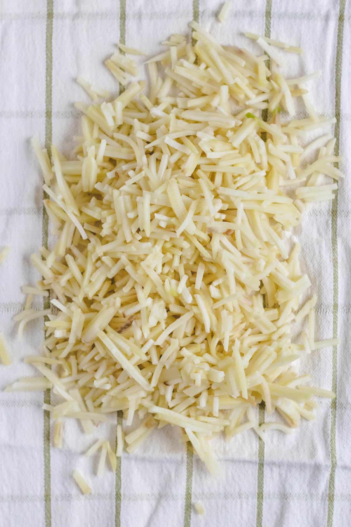 Uncooked hash browns on a kitchen towel to squeeze the moisture out of the potatoes.