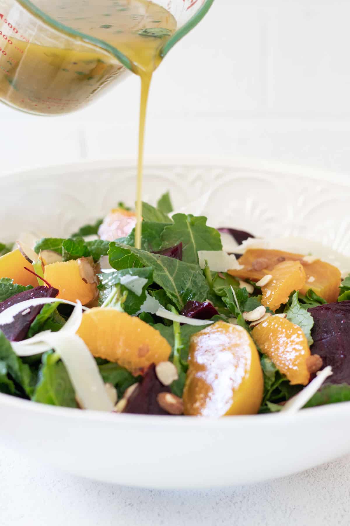 Pouring white balsamic dressing over top of a beet salad.