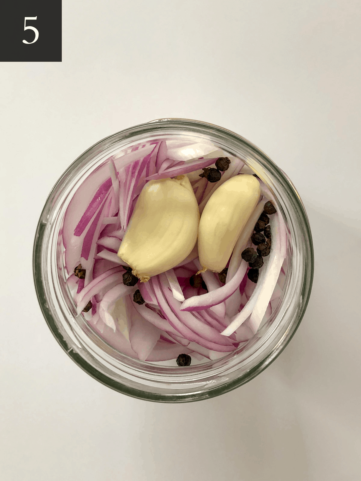 Overhead photo of onions, garlic, and peppercorns in a mason jar.