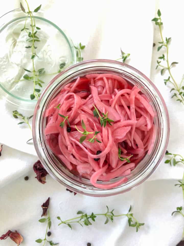 Overhead photo of pickled red onions in a mason jar with thyme leaves.