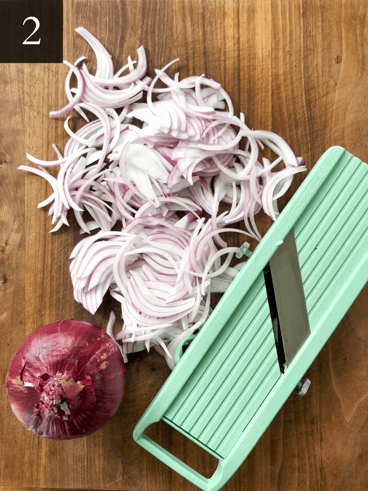 Thinly sliced red onion on a cutting board with a mandolin. 