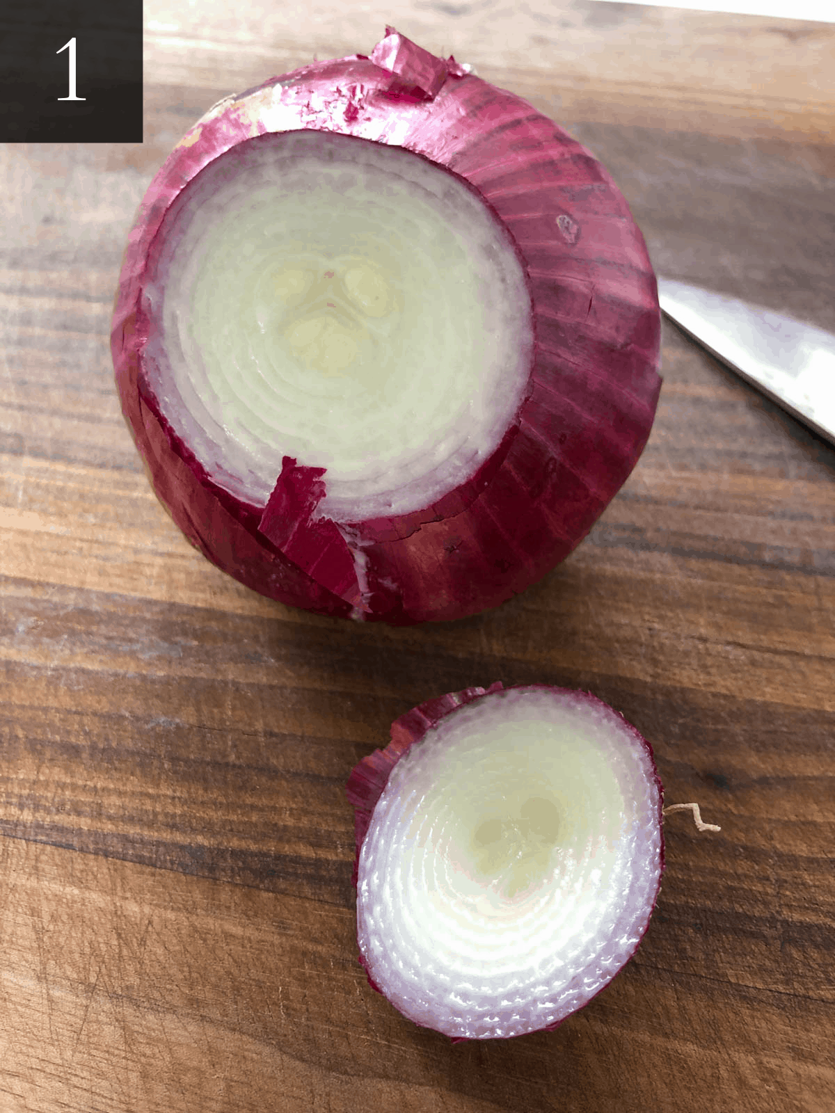 Cutting the top and bottom off of a red onion with a knife.