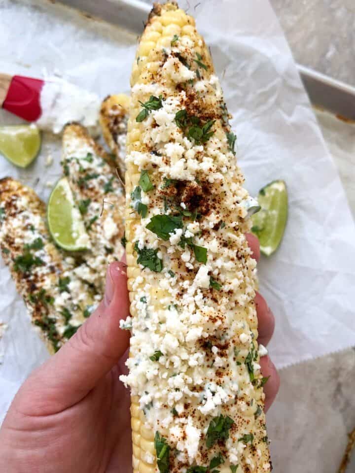 grilled mexican street corn holding in hands