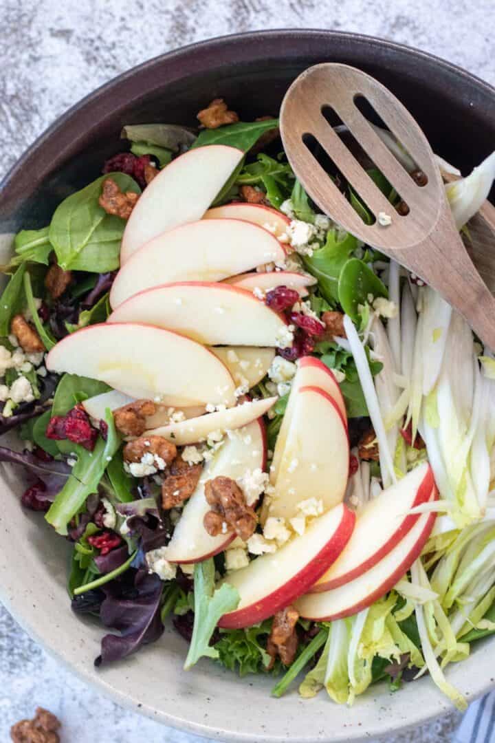 apple cranberry walnut salad in a large bowl with a wooden spoon