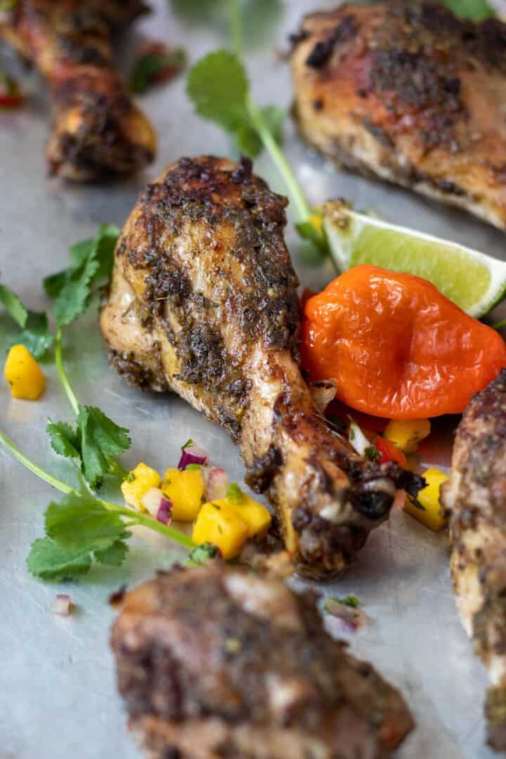 Jamaican Jerk Chicken on a baking tray with mangos and limes