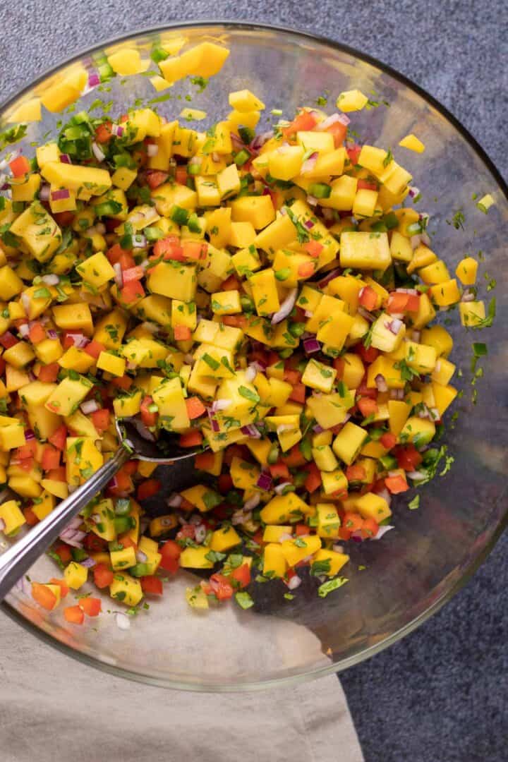 mixing mango salsa in a large mixing bowl with a spoon.