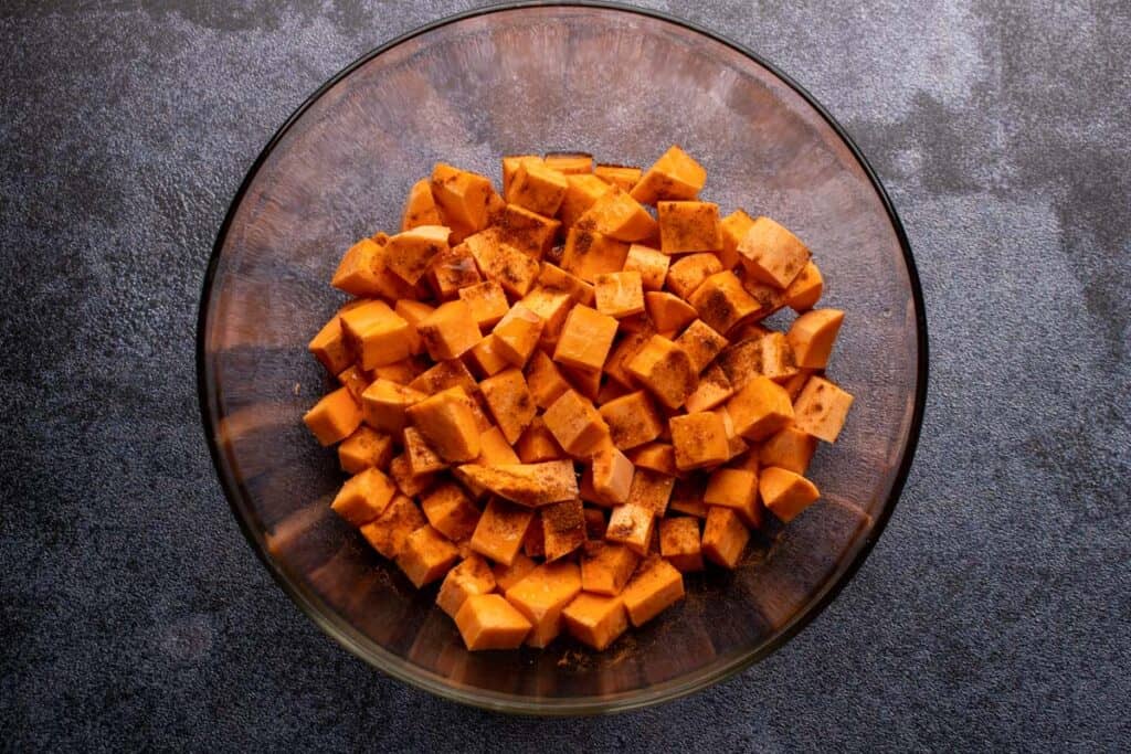Tossing sweet potatoes with seasonings in a large bowl.
