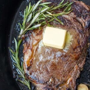 seared ribeye in cast iron pan with herbs and butter.