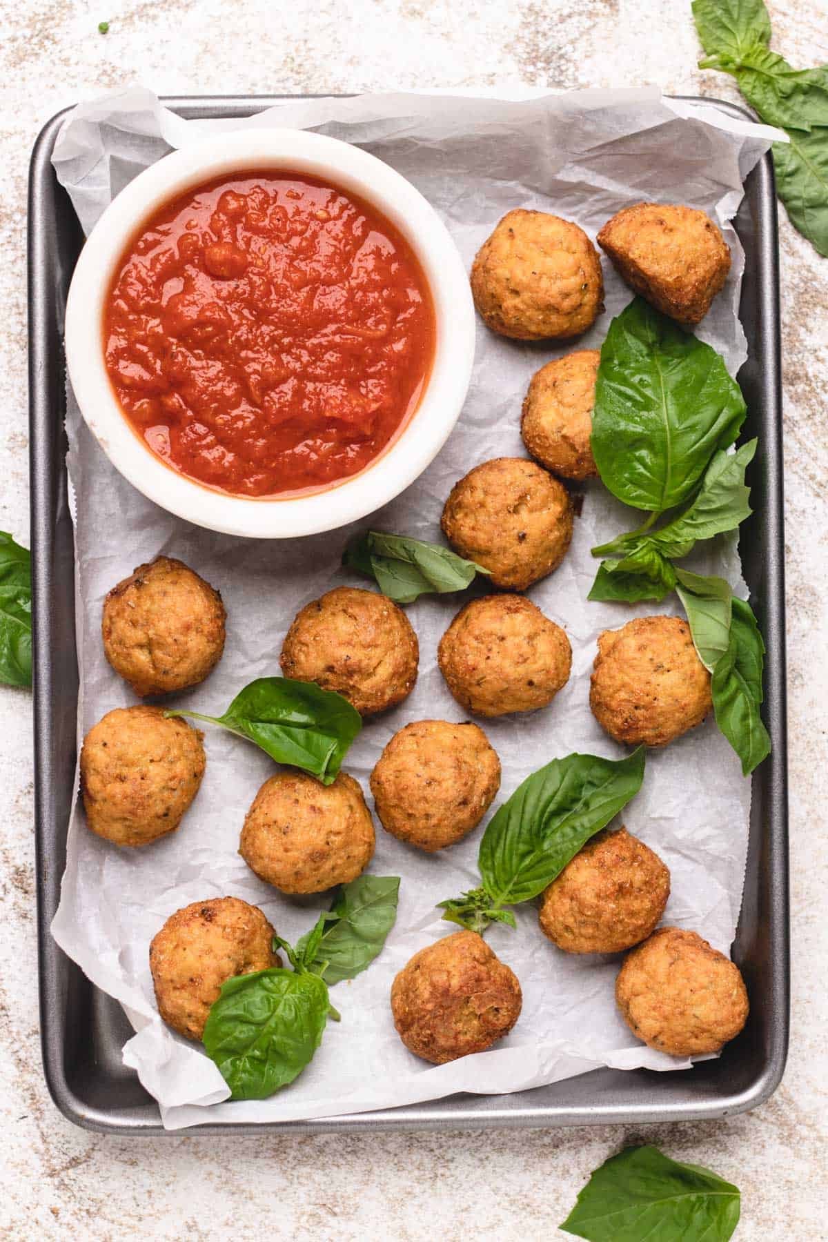 Meatballs on a baking tray with marinara sauce.