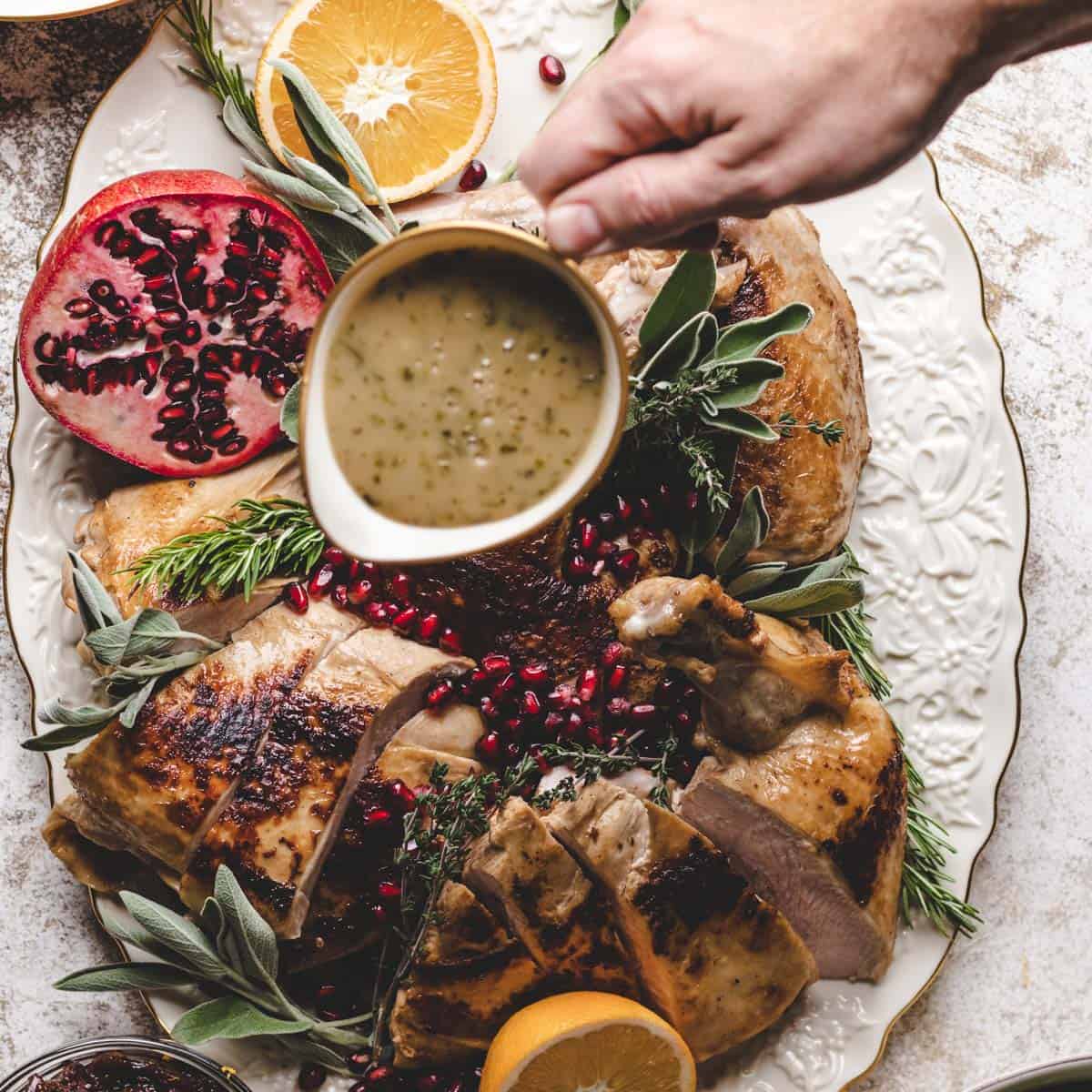 Pouring gravy over the top of the turkey.