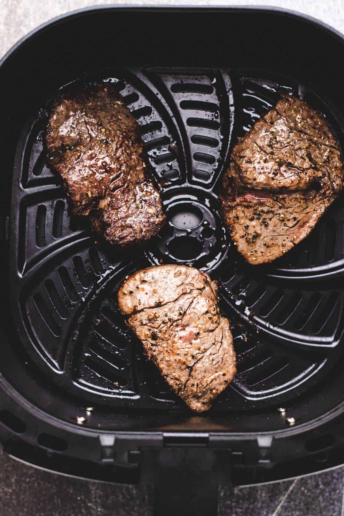 3 cooked filet mignons inside of an air fryer basket.