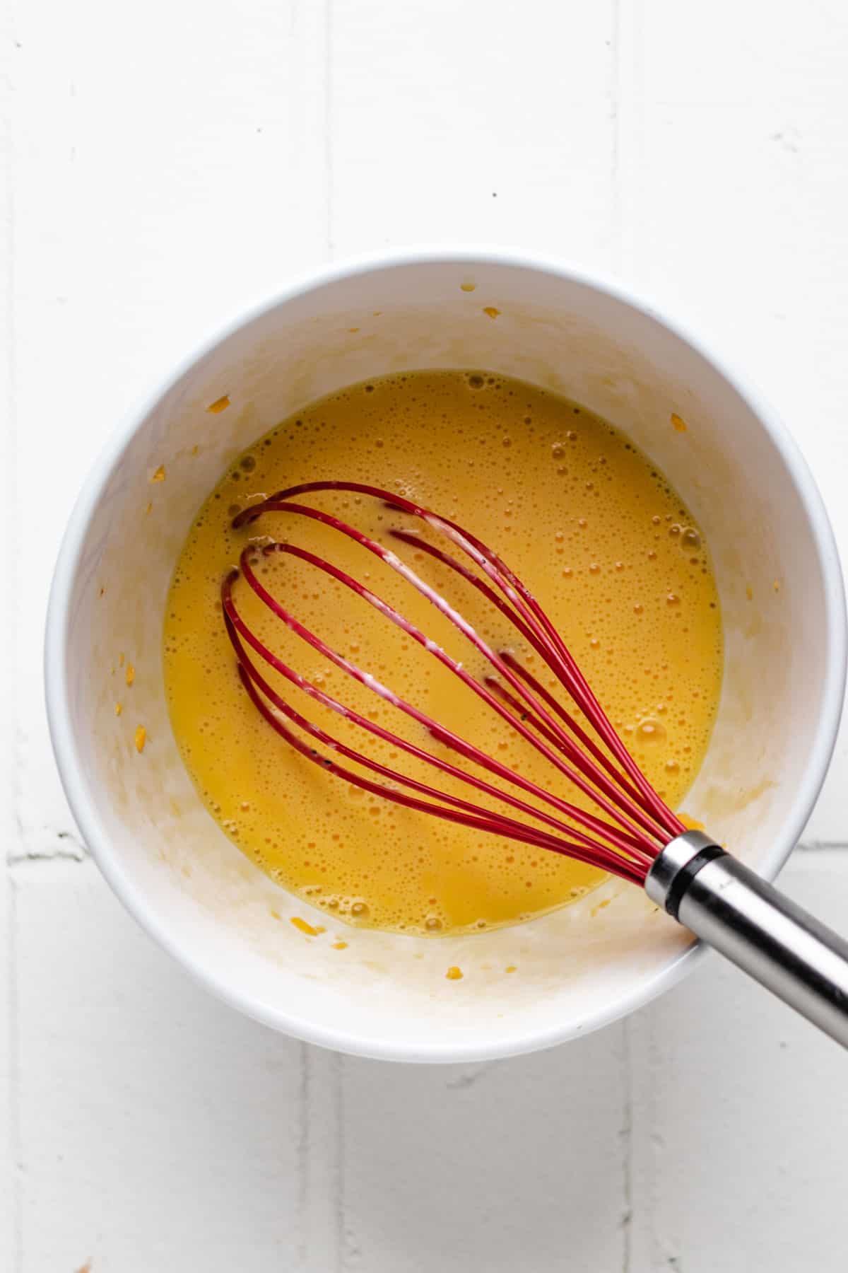 Hand mixing eggs in a white bowl using a whisk.