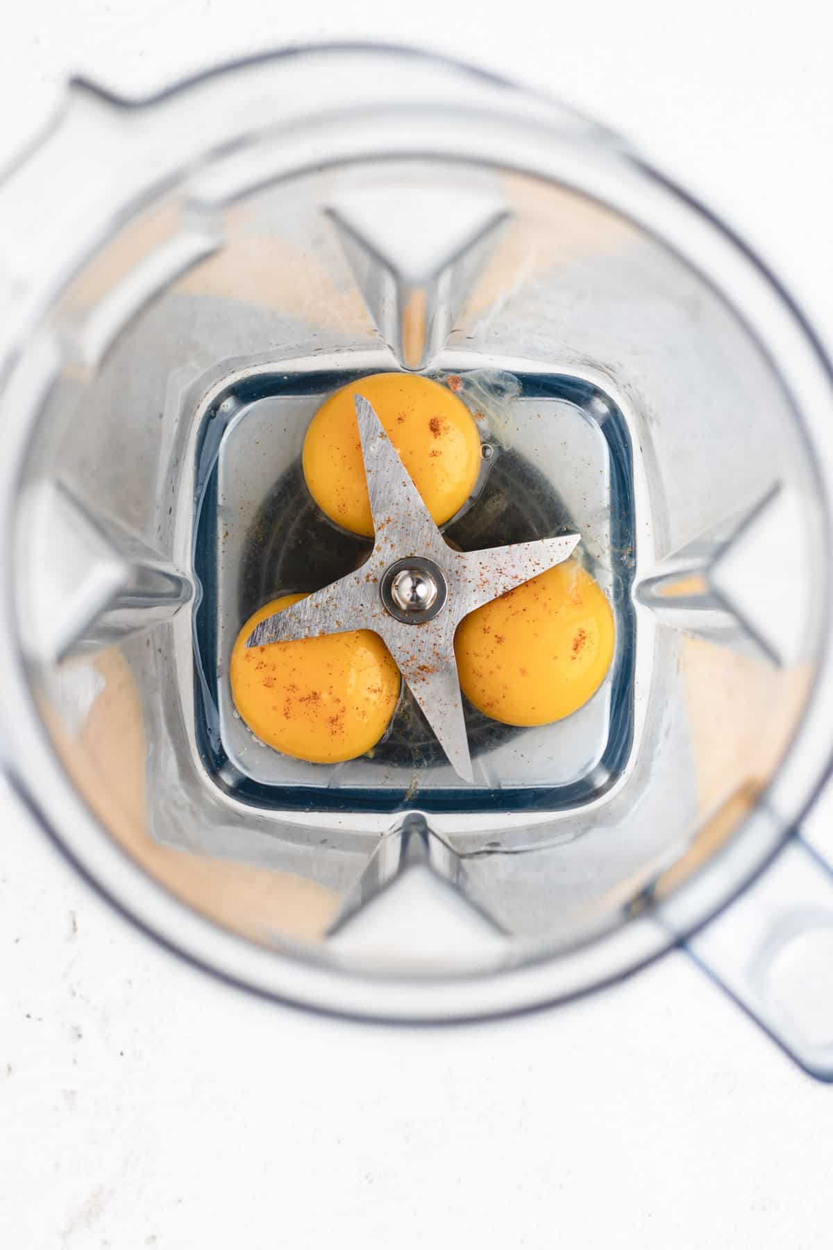 Image of a blender filled with a mixture of vibrant yellow egg yolks, tangy lemon juice, and a sprinkle of spicy cayenne pepper.