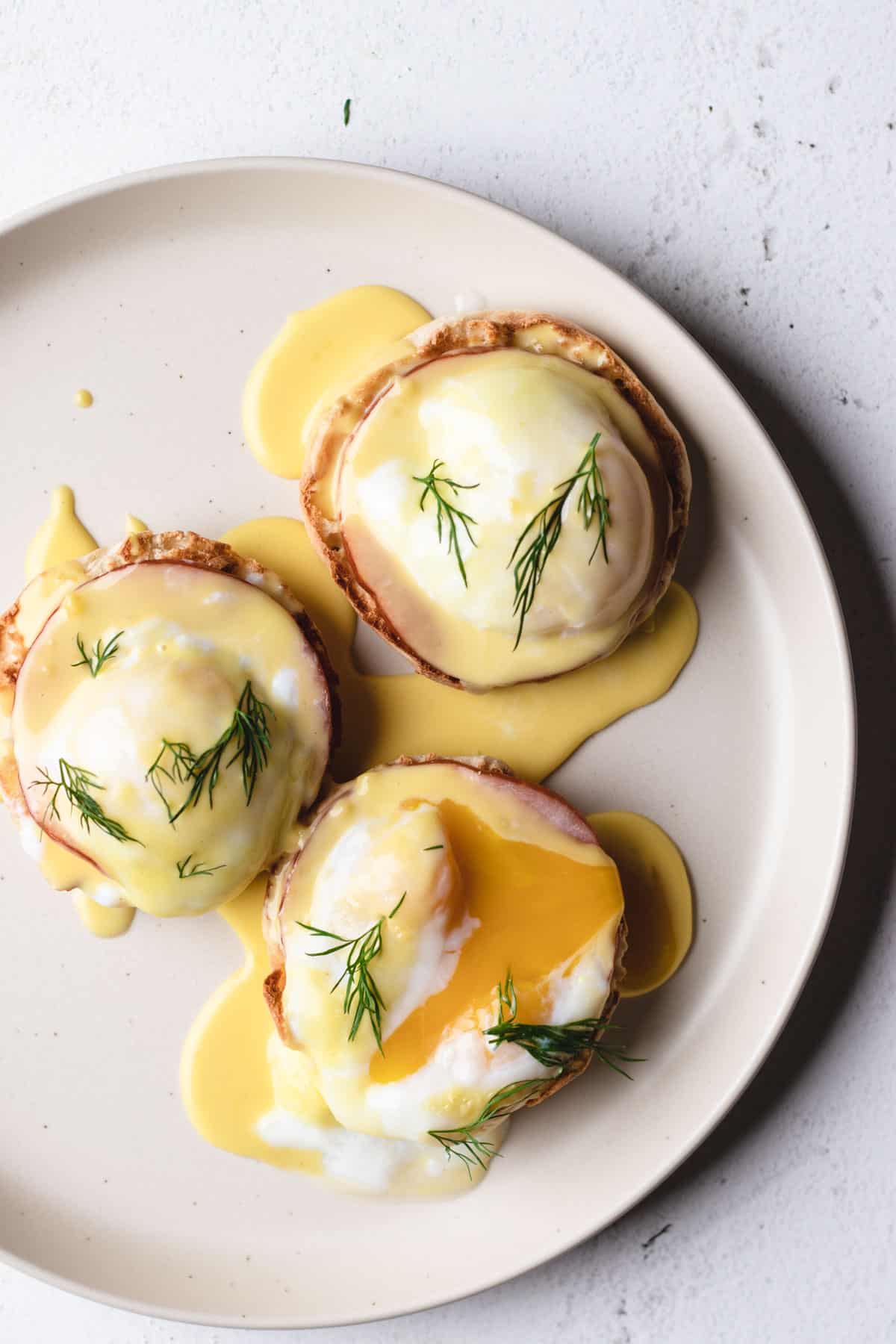 Threes eggs benedict on a large plate garnished with fresh dill.