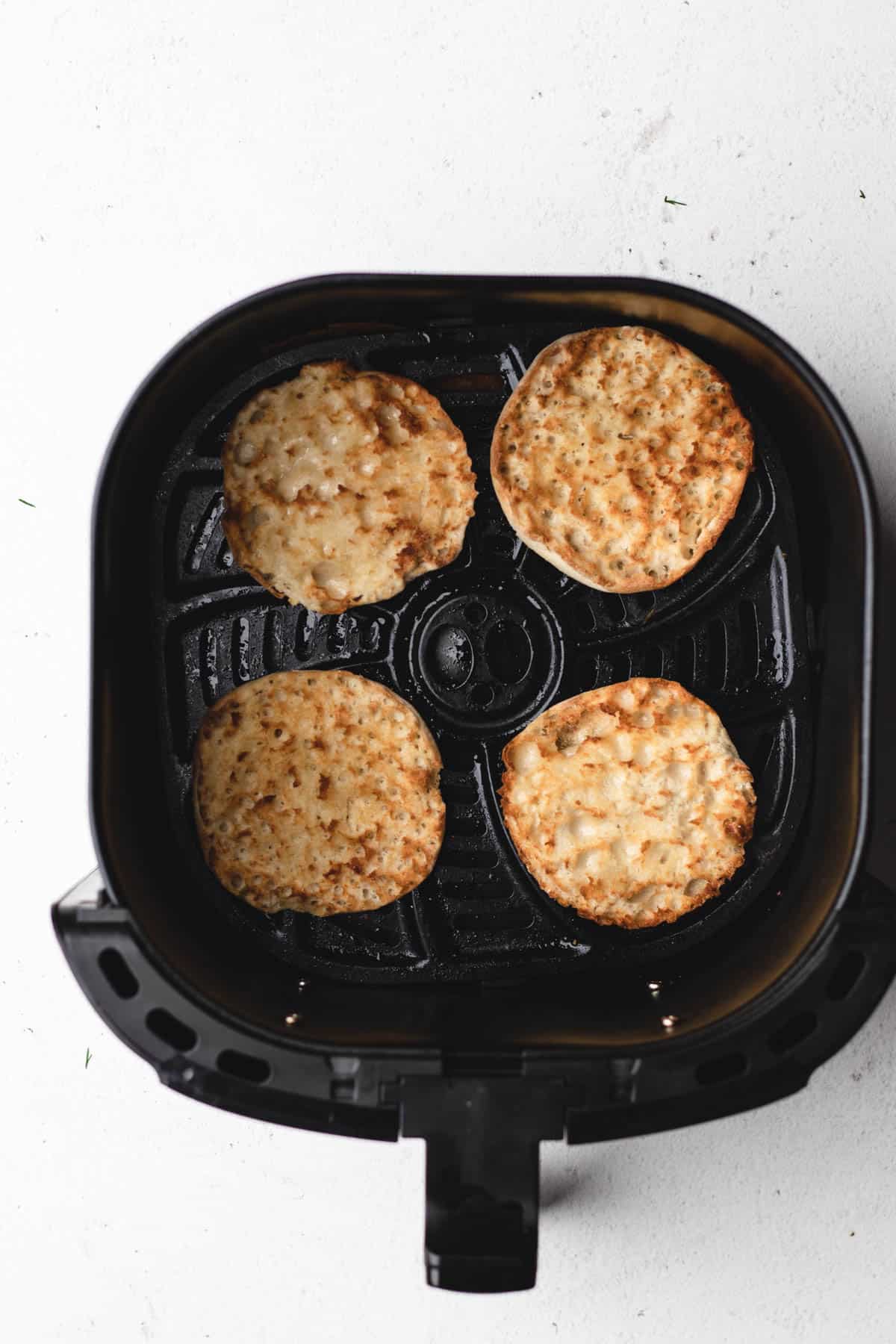 Toasting English muffins in an air fryer basket.