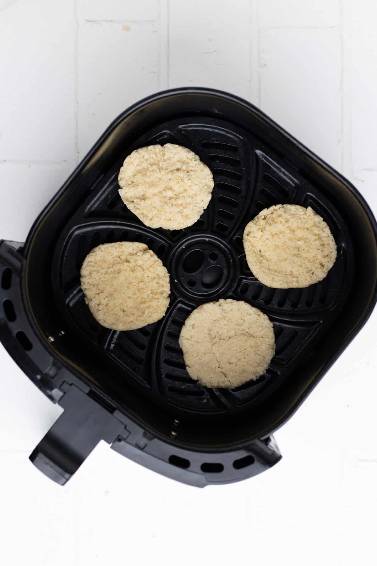 Four halves of untoasted English muffins in the air fryer.