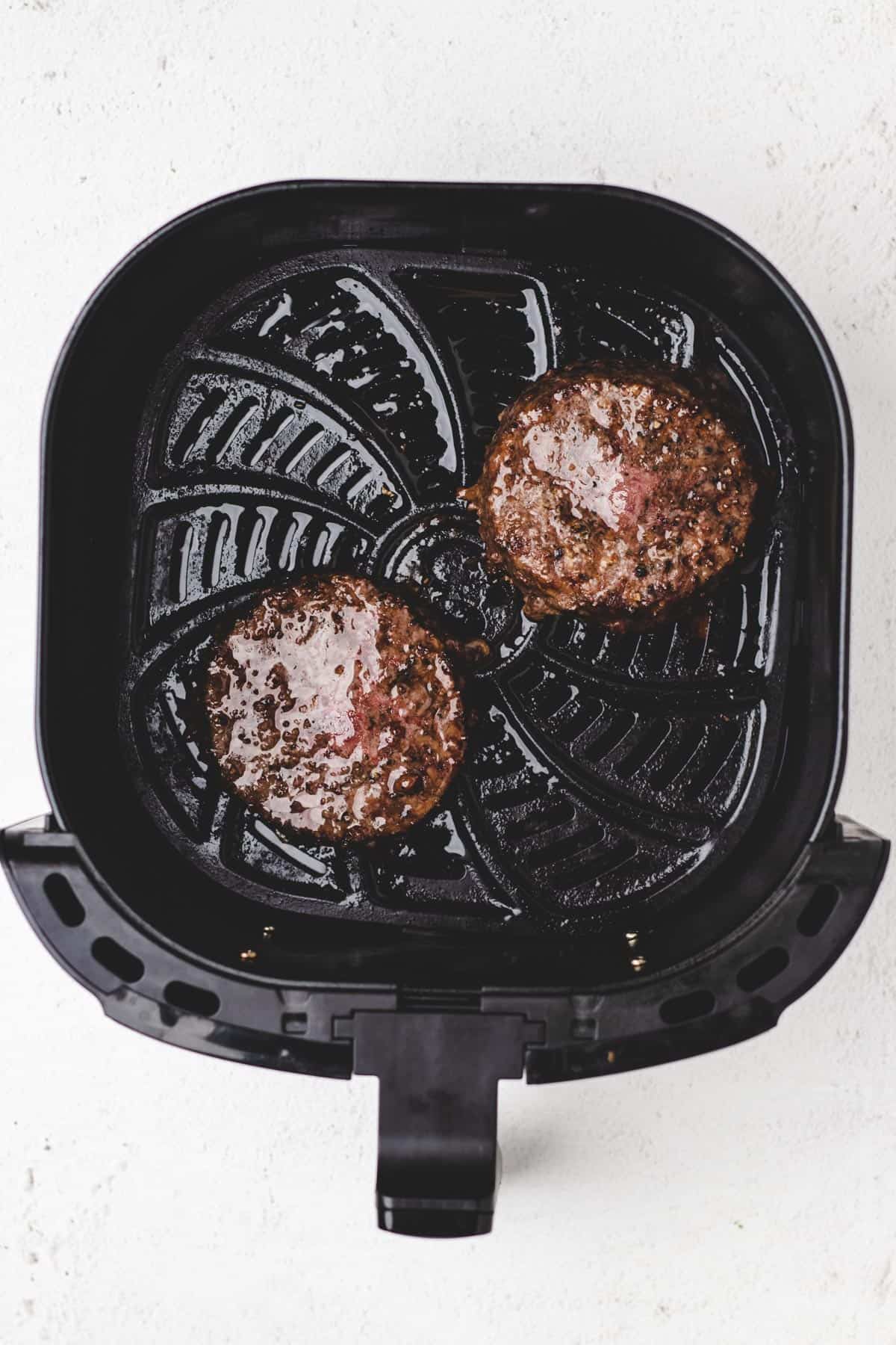 Cooked burgers in an air fryer basket.