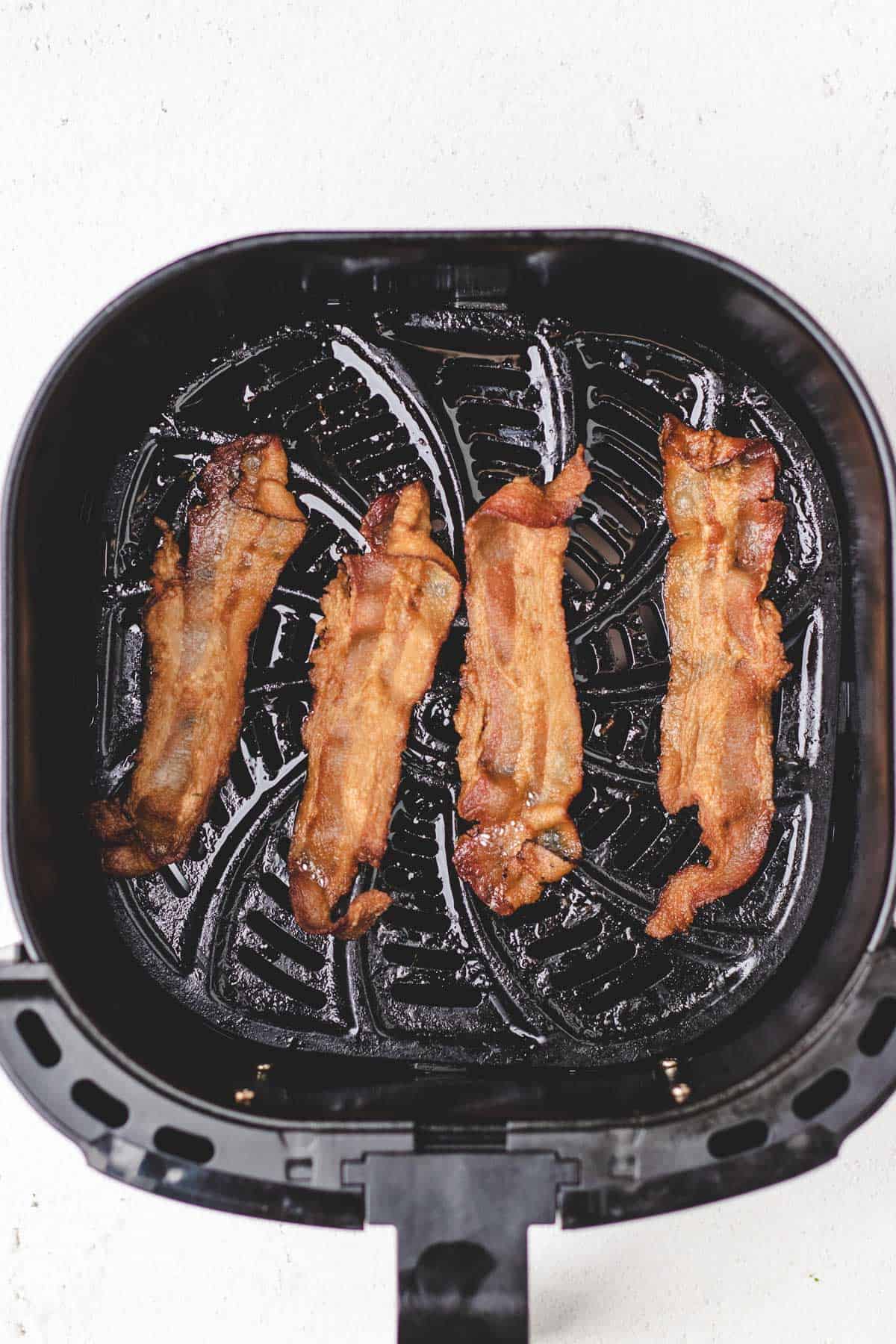 Cooked bacon in an air fryer basket.