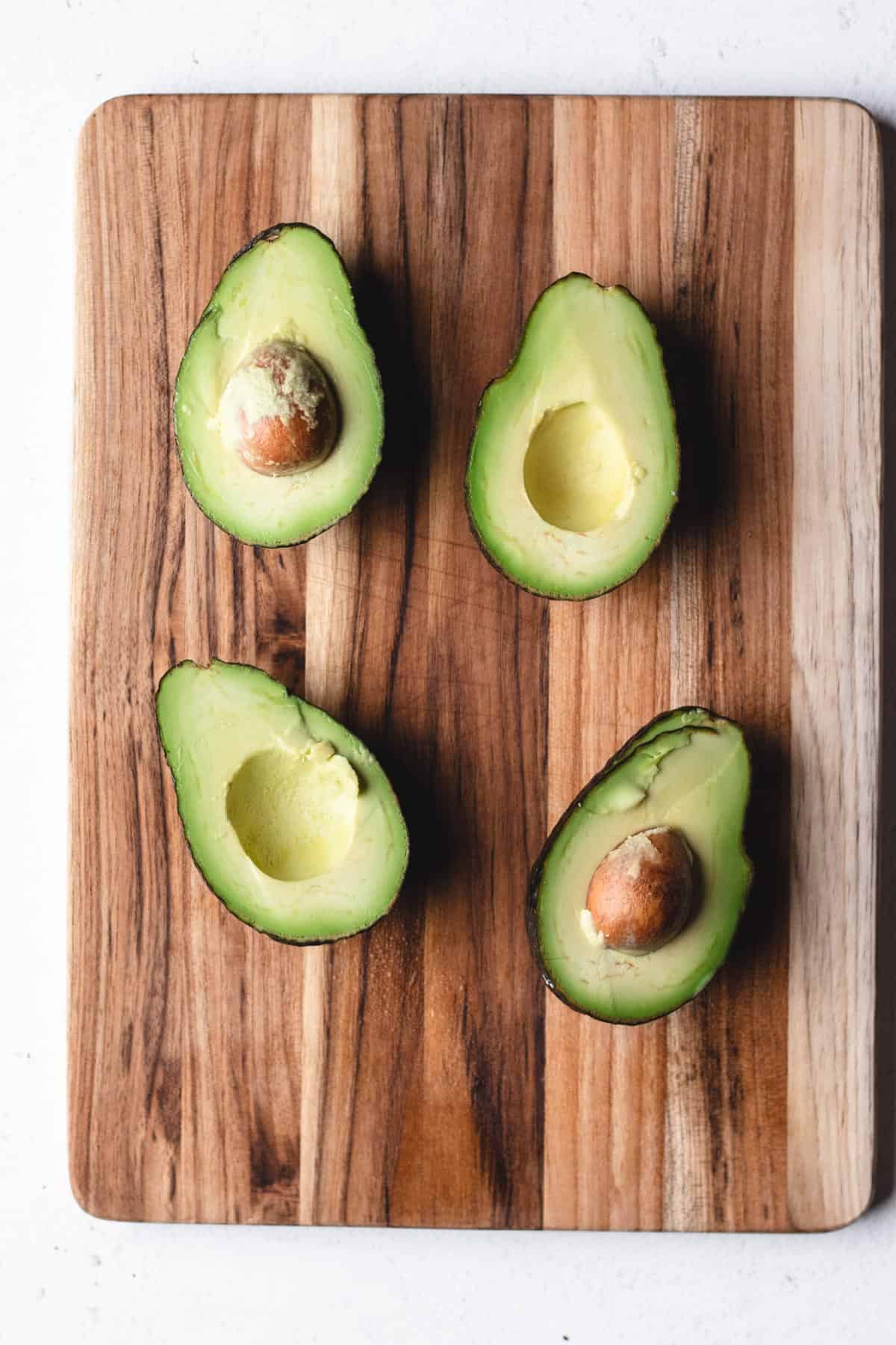 Avocado's cut in half on a wooden cutting board.