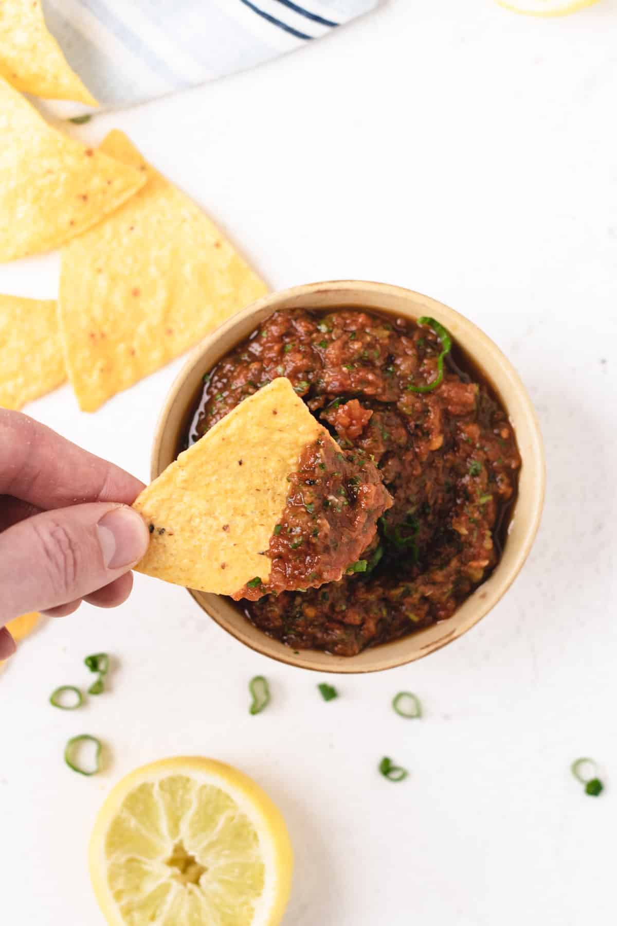 A photo of a hand holding a tortilla chip, dipping it into a small bowl of salsa.
