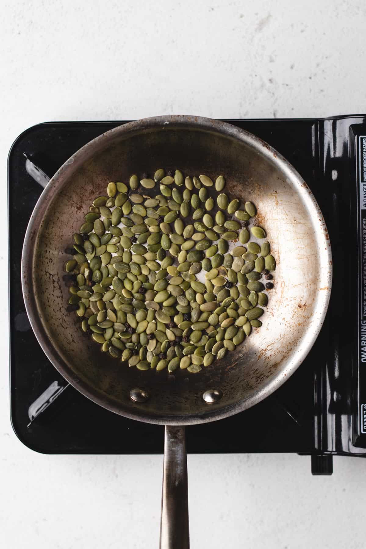 A photo of a pan with pepita seeds being toasted over a stove.