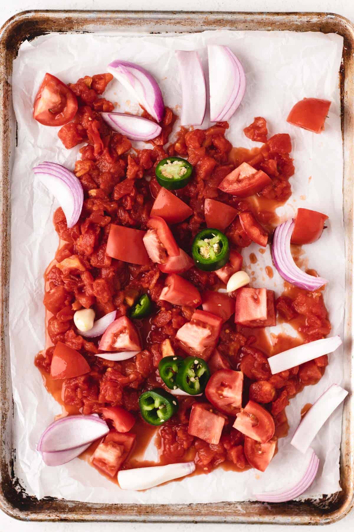 A sheet pan filled with salsa ingredients arranged in a single layer, ready to be roasted in the oven.