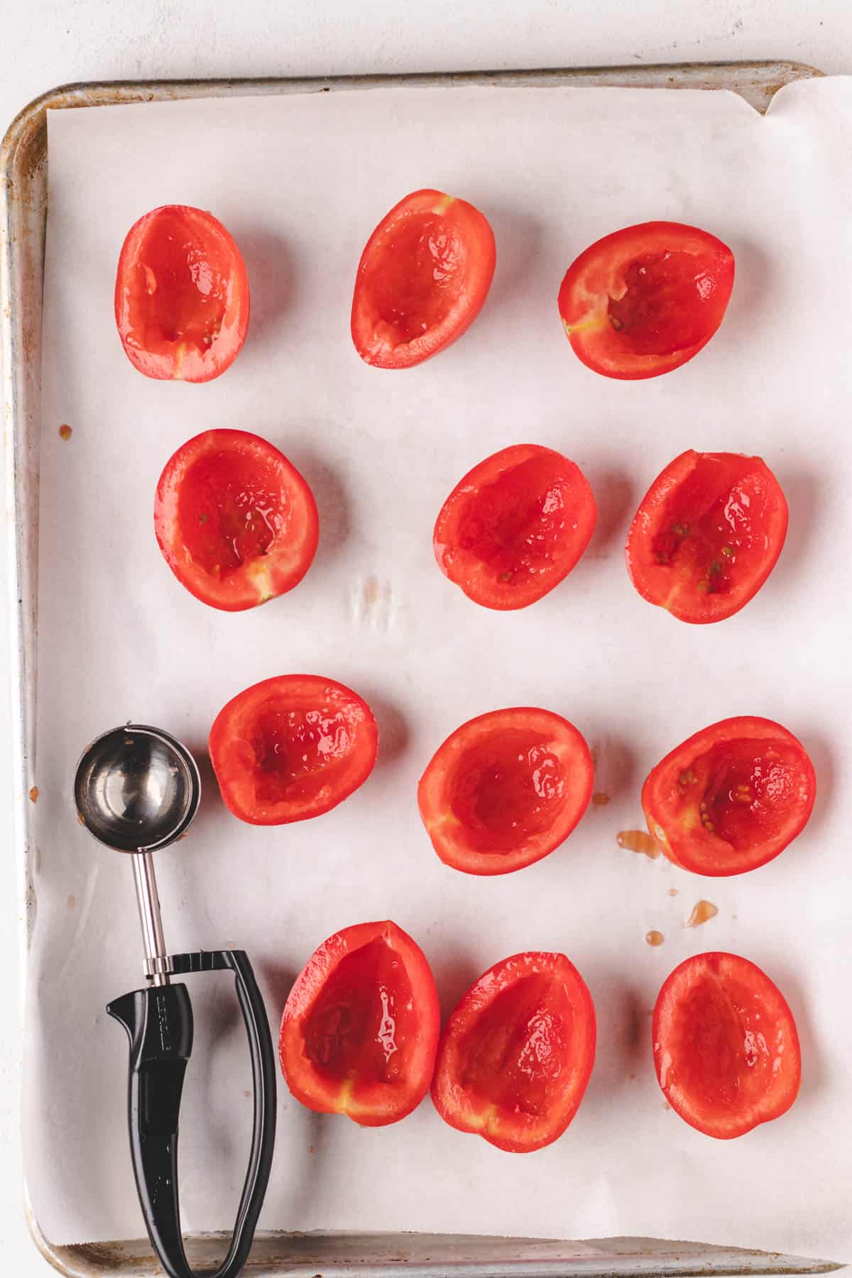 Roma tomato halves on a baking tray with tomato seeds removed.