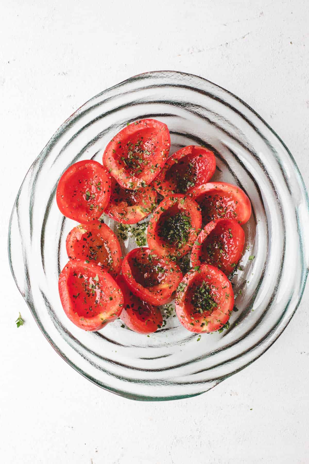 Tomatoes that have been sliced and tossed in a large bowl with olive oil, fresh thyme, salt, and pepper.