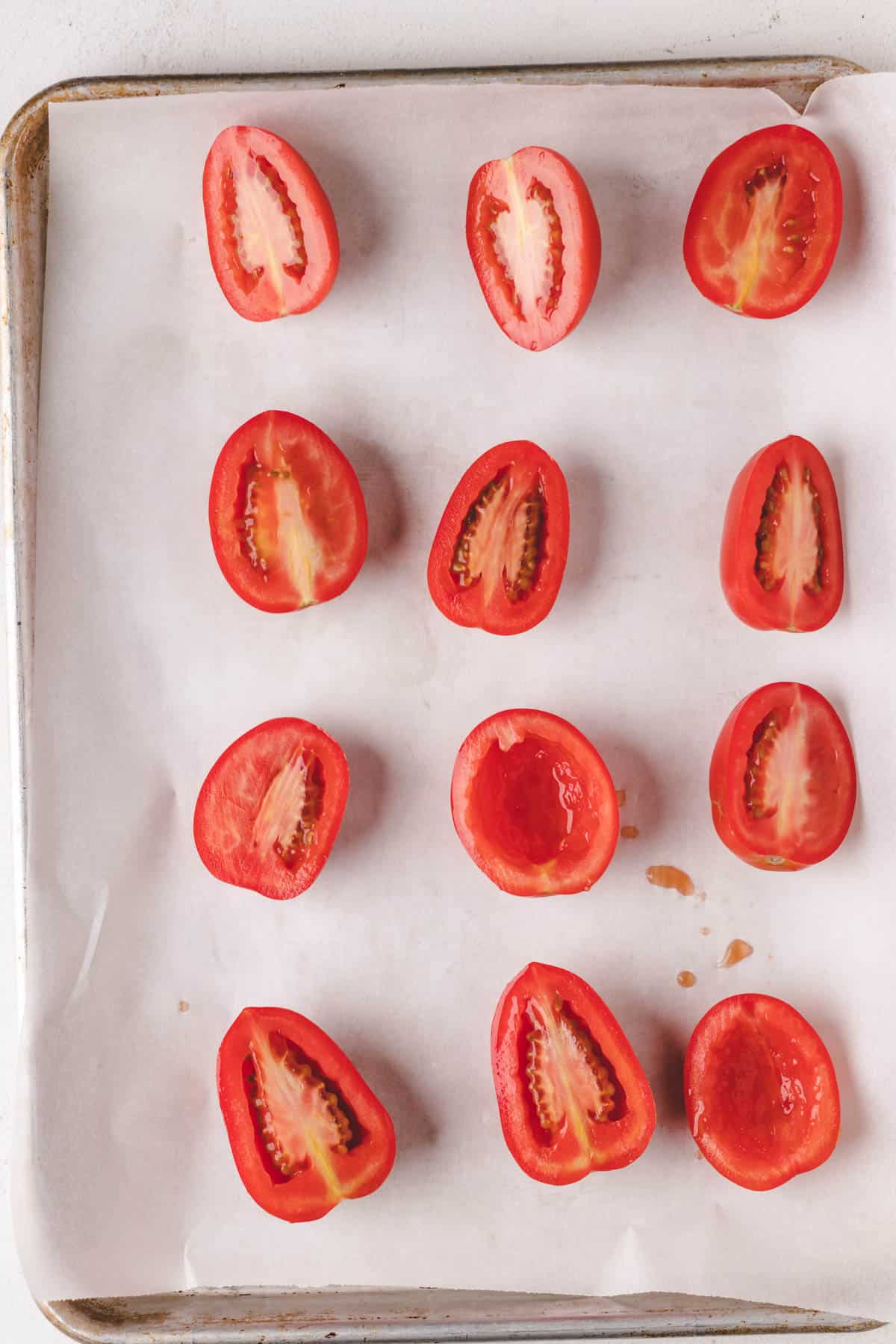 Roma tomatoes that have been cut in half and are placed on a baking tray, ready for slow roasting.