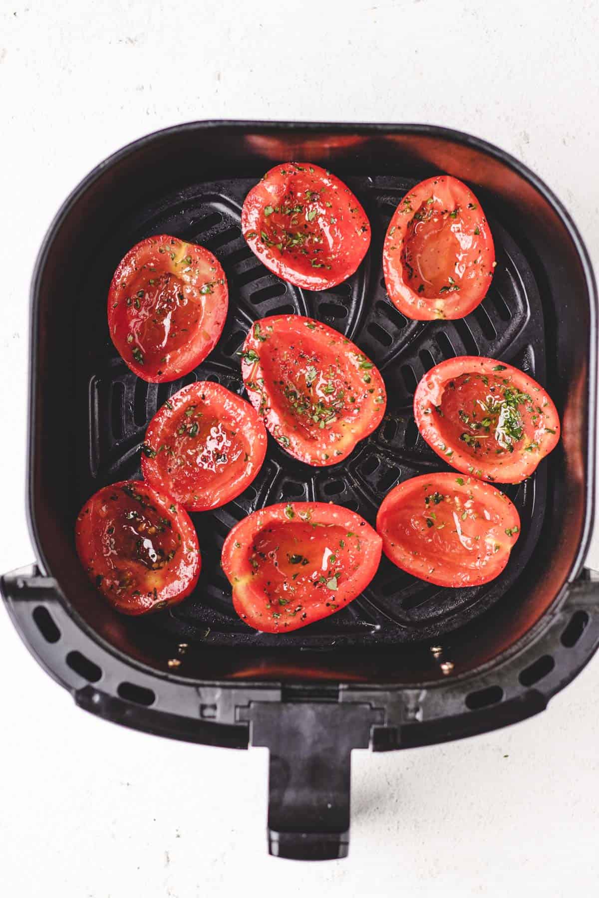 Raw tomato halves arranged in an air fryer basket, ready for slow roasting.