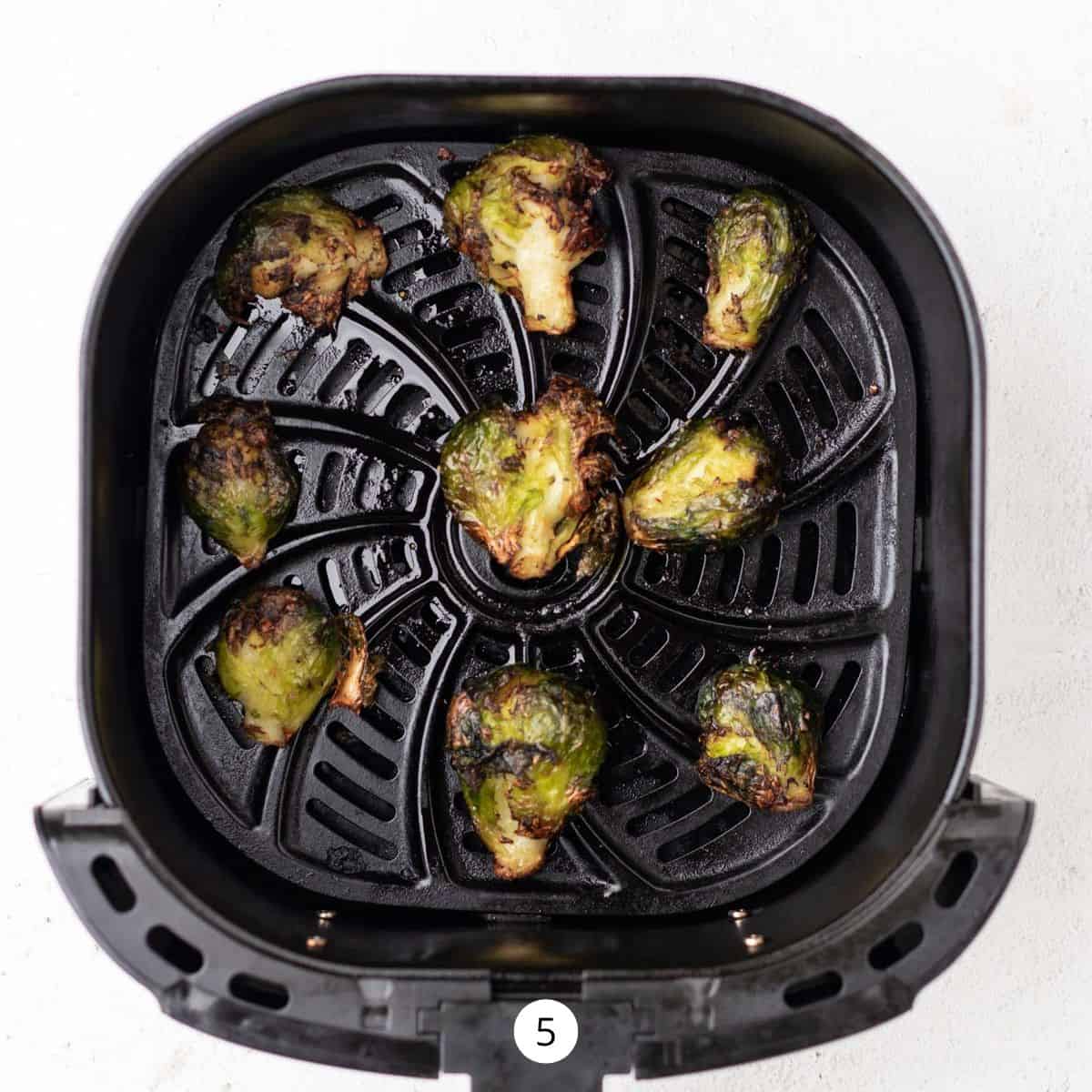 Cooked smashed Brussels Sprouts in an air fryer basket.