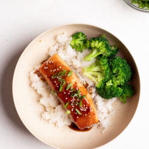 Teriyaki salmon, white rice, and broccoli in a round bowl.