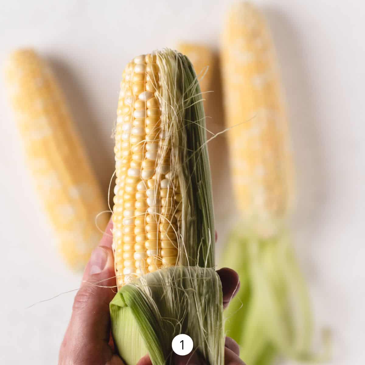 Shucking one ear of corn, by peeling back the husk.