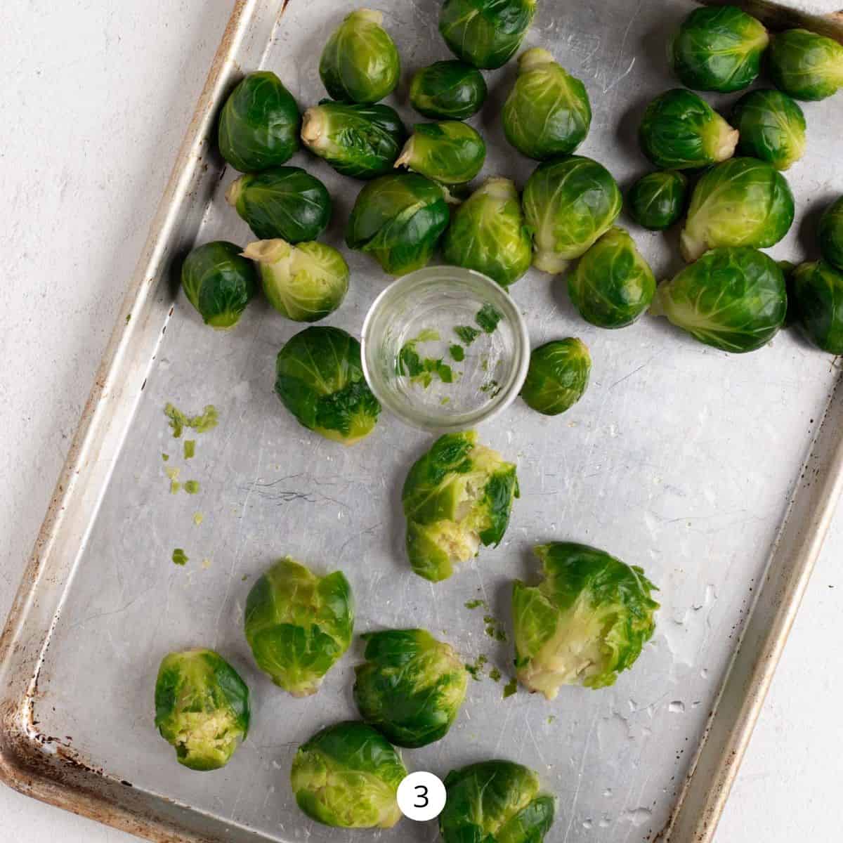 Smashing Brussels Sprouts with a mason jar on a half sheet pan.