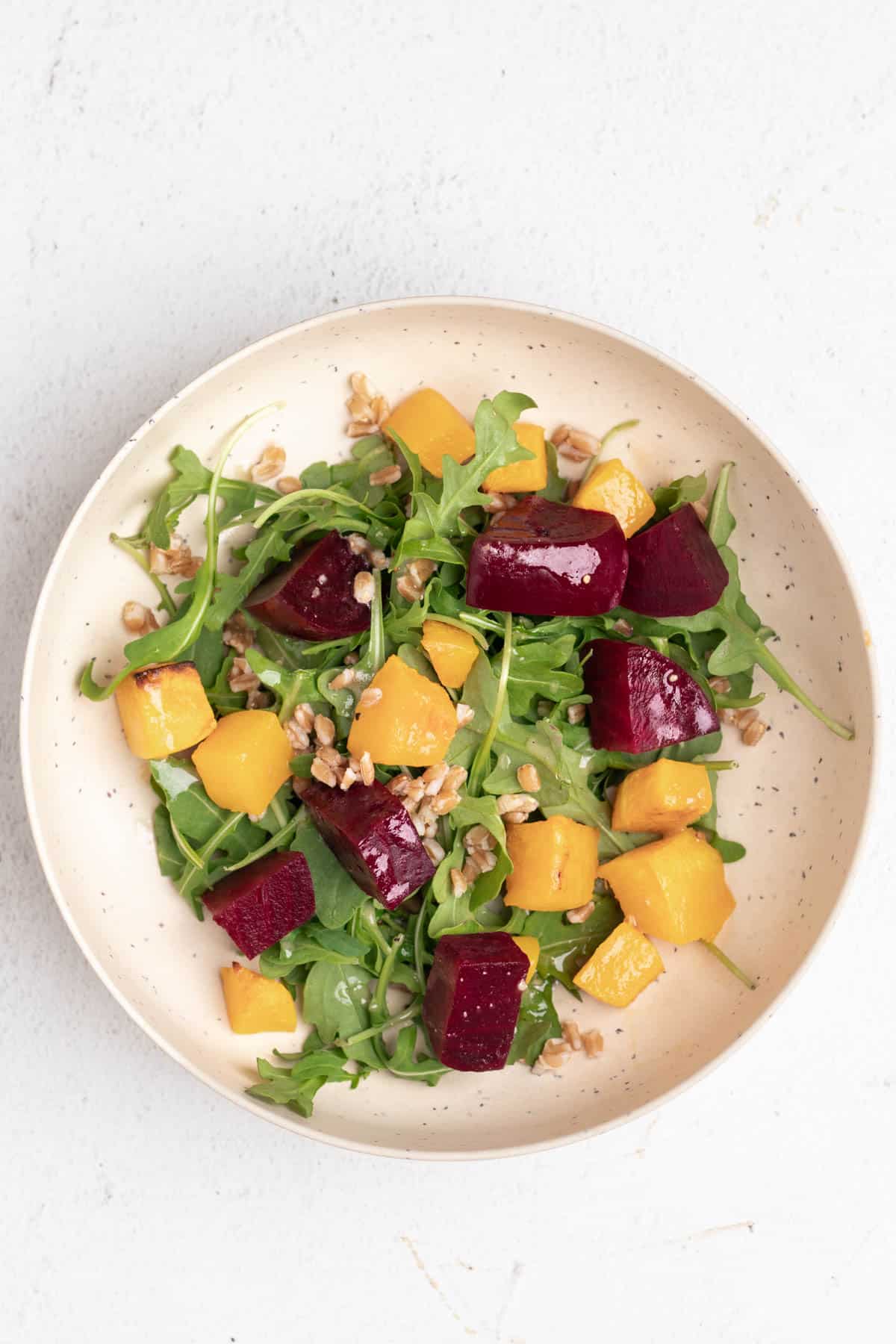 A salad of beets, butternut squash, arugula, and faro inside of a salad bowl.