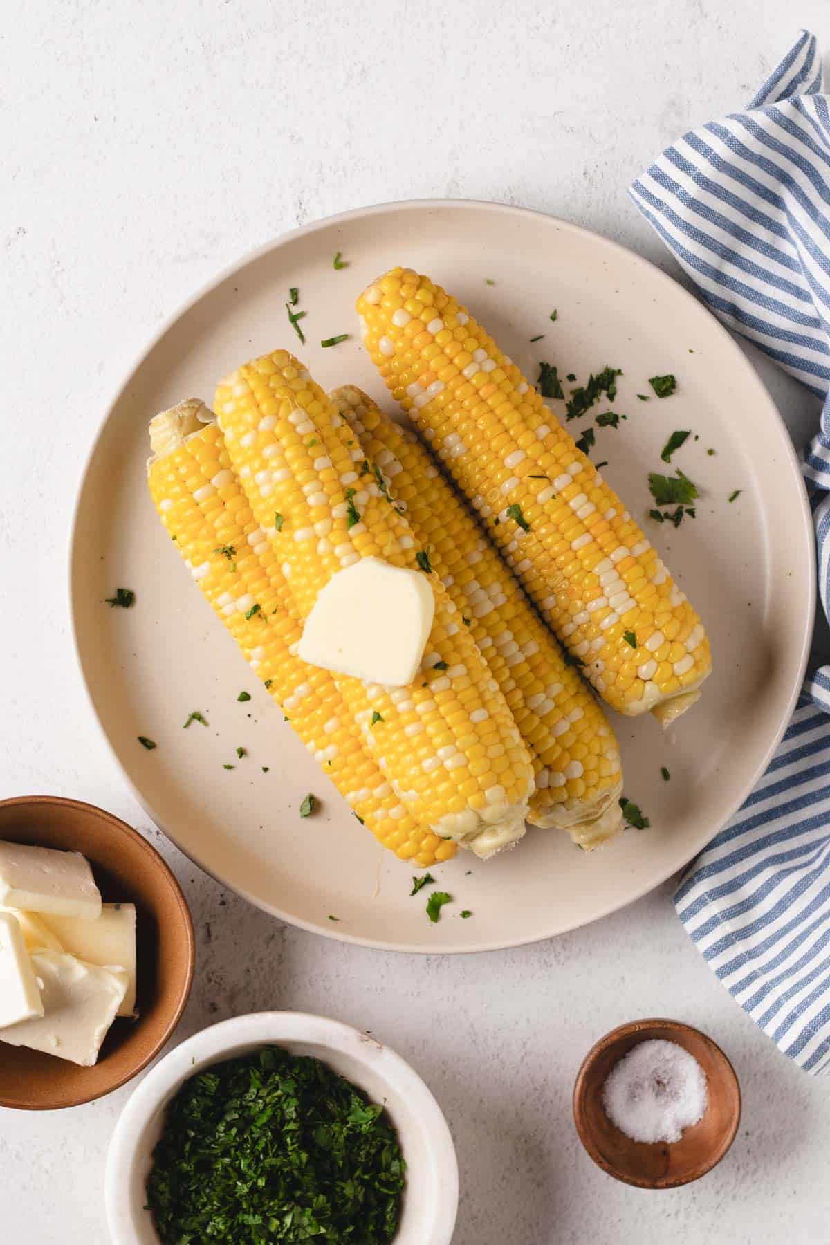  four ears of sous vide corn on a cob on a white plate with butter and cilantro.