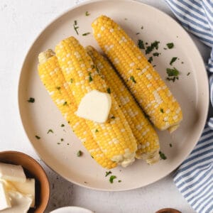 Sous vide corn on the cob on a large round plate with butter and cilantro.