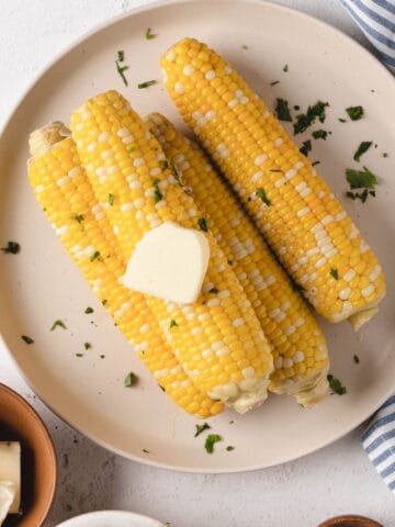Sous vide corn on the cob on a large round plate with butter and cilantro.