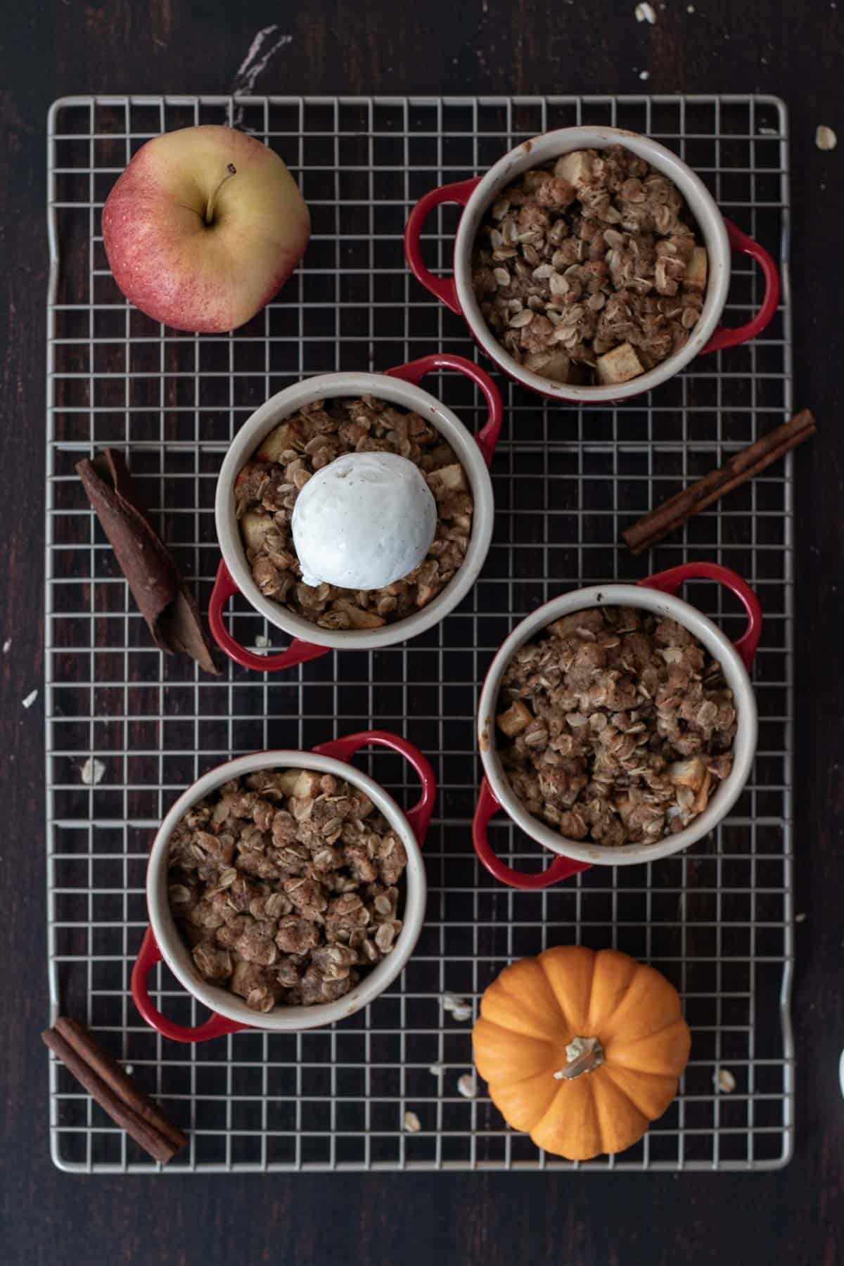 Four small apple crisp's on a wire baking rack with a scoop of vanilla ice cream on top.