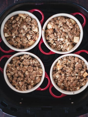 Mini apple crisp being cooked inside of an air fryer basket topped with an oatmeal topping.