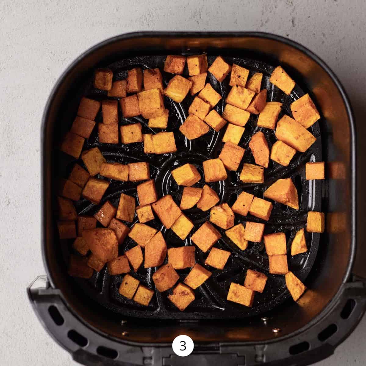 Roasting cubed butternut squash inside of a air fryer basket.