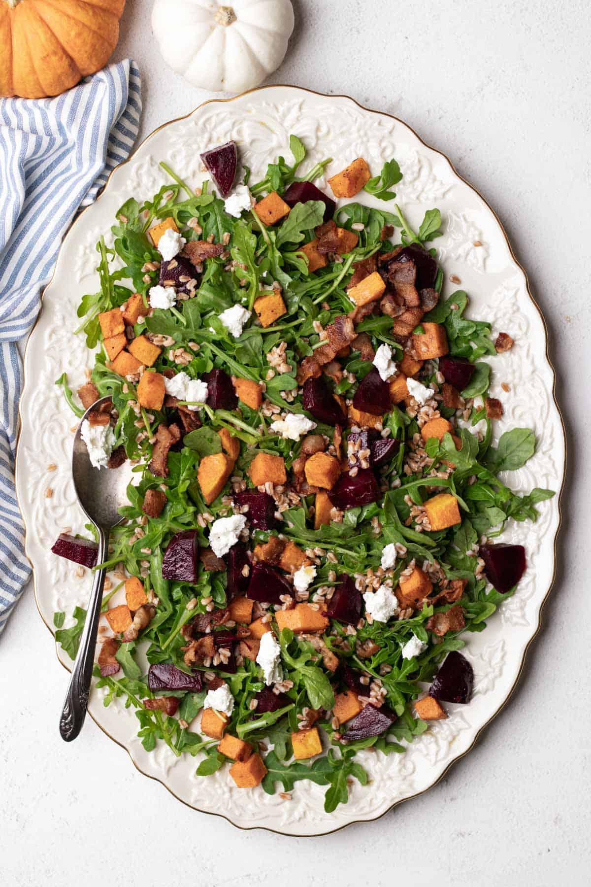 An oval platter with arugula, butternut squash, and beet salad with a serving spoon.