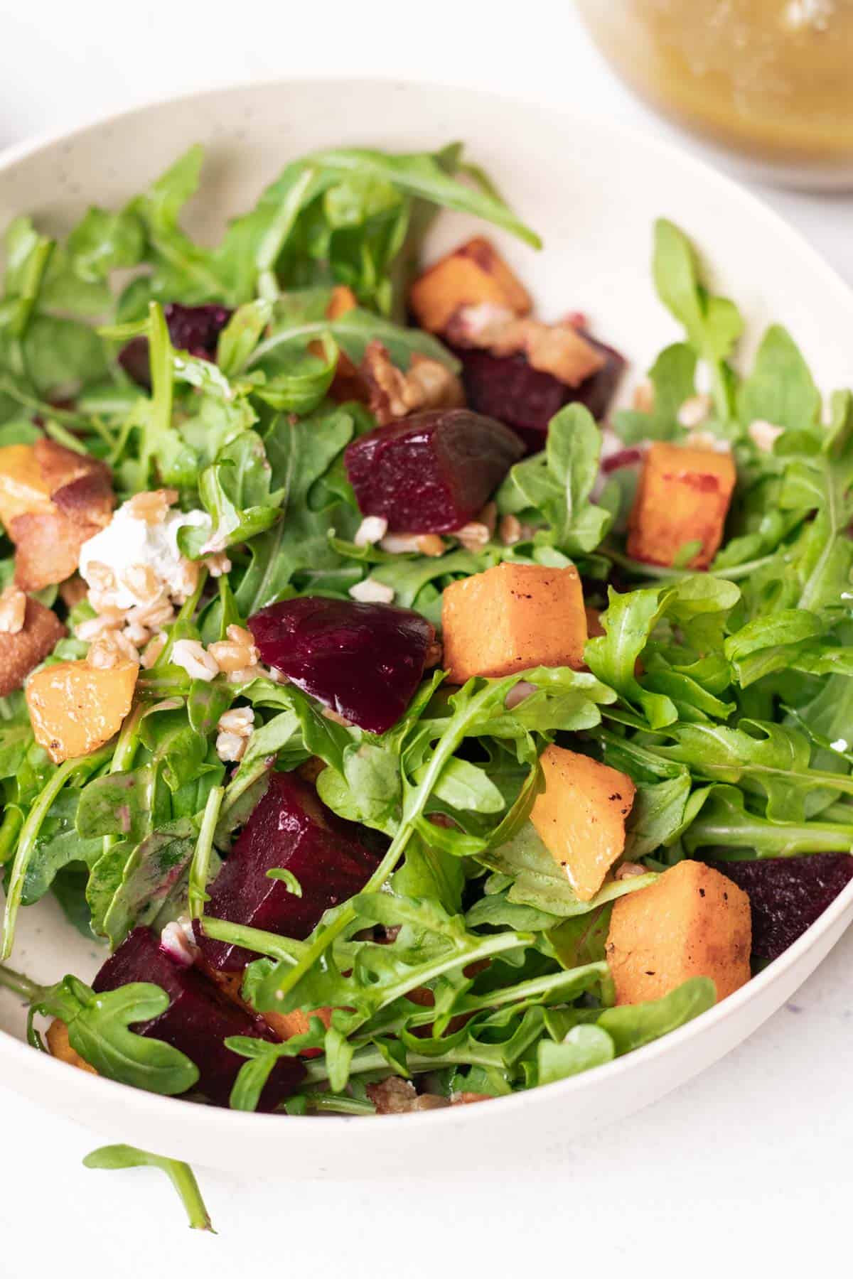 Arugula salad with beets, and butternut squash in a round salad bowl.