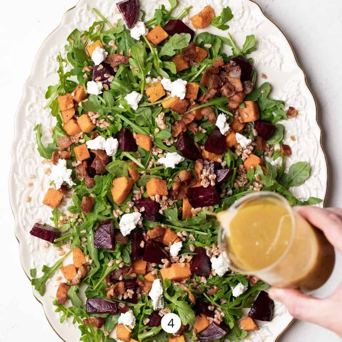 Pouring a maple-dijon dressing over top a butternut squash and beet salad on a large oval platter.