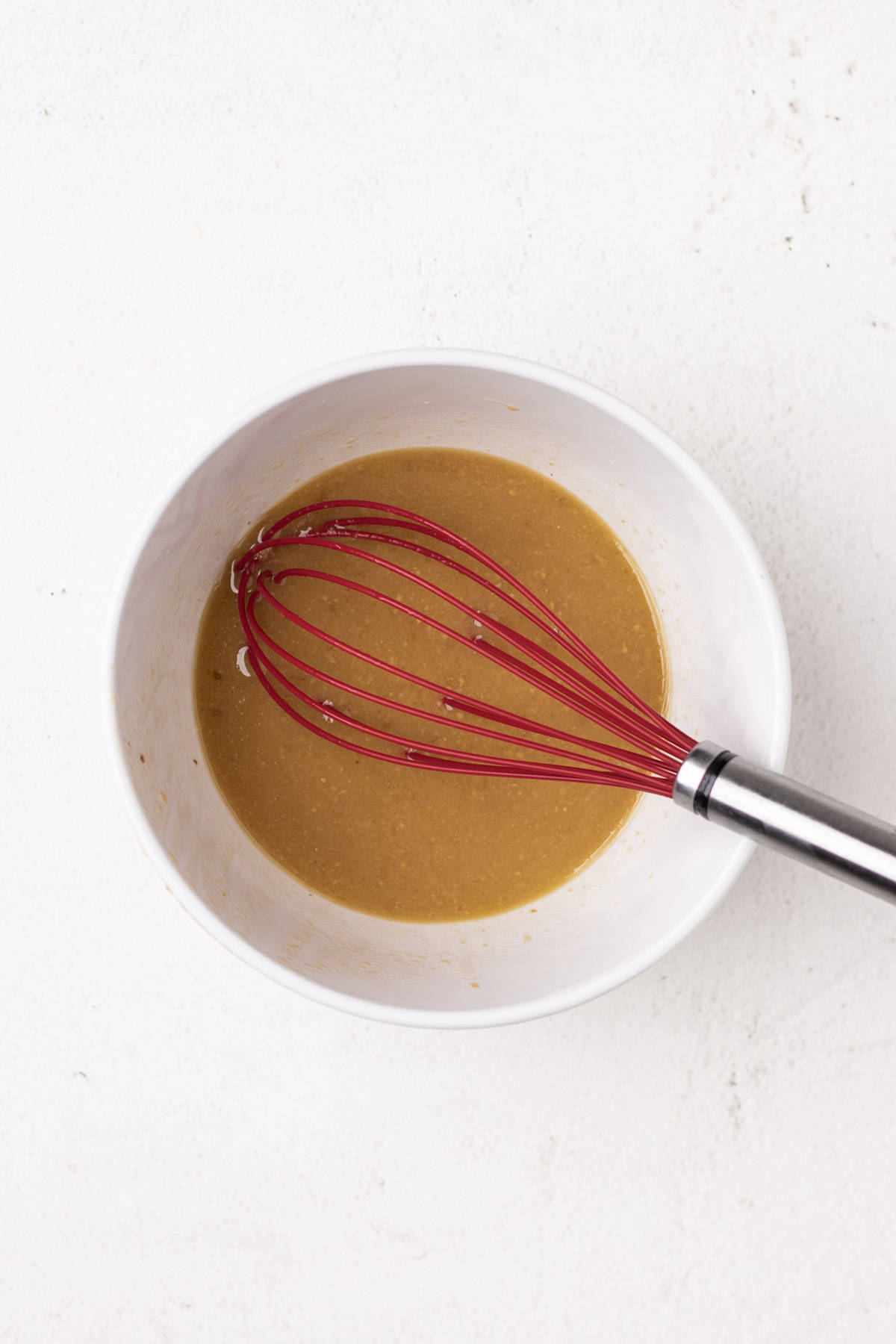 Using a red whisk to mix the Maple Dijon vinaigrette together in a round white bowl.