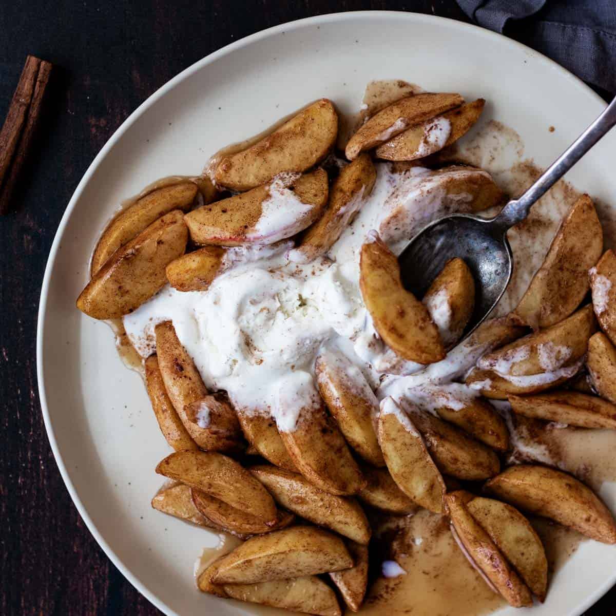 Two slices of caramelized apples on a spoon with vanilla ice cream.